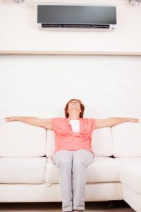 Woman escapes from the heat under the air conditioner at home. Happy mature woman on sofa