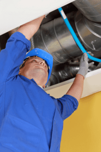 Technician raising hand above head while cleaning air ducts above inside roof