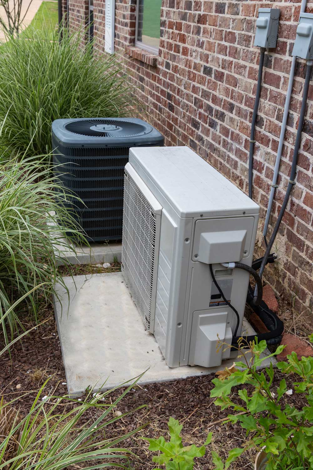 HVAC Air Conditioner Compressor and a Mini-split system together next to each other, next to a brick home.