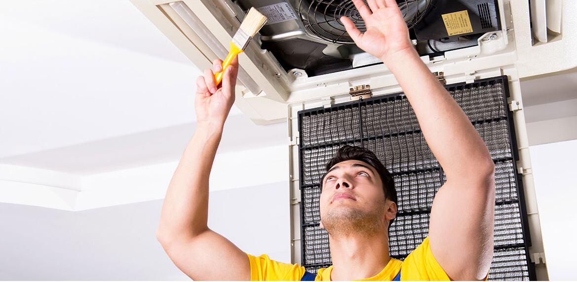  A man holds a cleaning tool, preparing to clean a ceiling fan in a well-lit room.